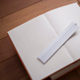 An open blank notebook with cream-colored pages and a white divider sheet, resting on a wooden surface.