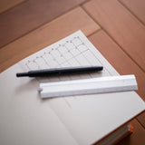 A black pen and a white ruler resting on an open notebook with a calendar page, placed on a wooden surface.